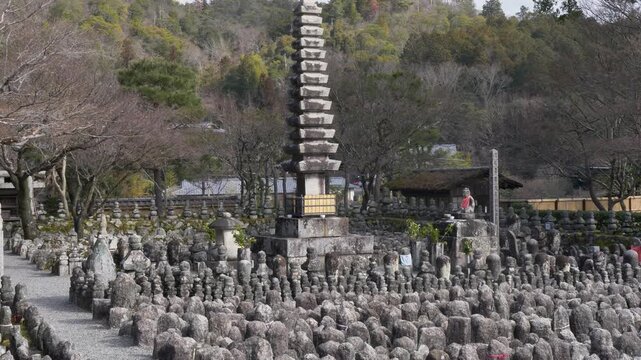 Slow motion landscape of historic stone statues lined up with a sacred pagoda monument in the courtyard grounds of Adashino Nenbutsuji temple shrine in Kyoto Ukyo Ward Japan Asia tourism and travel