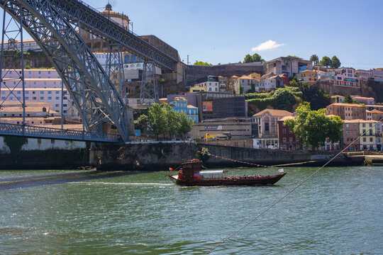 Aerial view of the Dom Luis I Bridge casting shadows on the Douro River as a traditional Rabelo boat glides through the water, Porto, Porto District, Portugal.