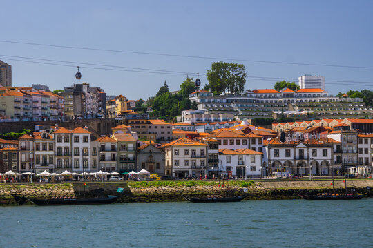 Aerial view of the red-tiled roofs cascade down to the Douro River, where boats bob gently, framed by the iconic cable cars against a clear sky, Porto, Porto District, Portugal.