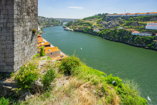 Aerial view of the Douro River snaking through the city, bordered by ancient stone walls and lush greenery, revealing the Dom Luis I Bridge in the distance, Porto, Porto District, Portugal.
