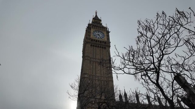 Big ben clock tower silhouette against a cloudy sky in london, a famous landmark of the united kingdom showing architectural details and the iconic clock face against the sun