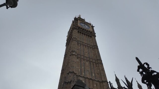 Big ben clock tower rising against a cloudy sky in london, a famous english tourist landmark and symbol of the united kingdom, revealing decorative iron fence elements
