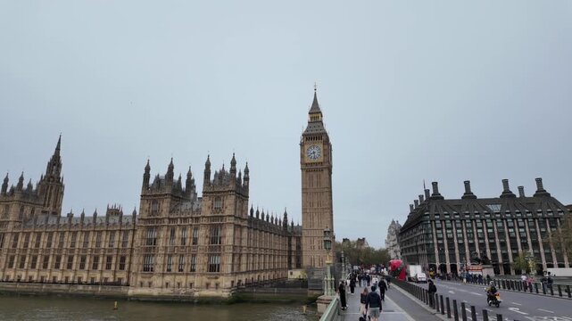 People walking on westminster bridge viewing the houses of parliament and big ben on a cloudy day in london, representing uk politics, tourism, and british culture