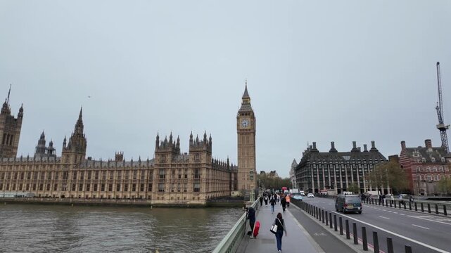 Famous big ben clock tower and houses of parliament on river thames seen from westminster bridge with people walking and traffic including a classic red double-decker bus