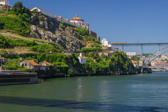 Aerial view of the Douro River winding past the Vila Nova de Gaia cliffs and Dom Luis I Bridge under a bright sky, Porto, Porto District, Portugal.