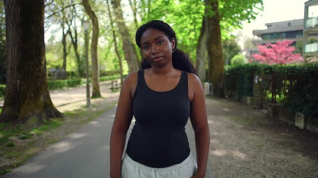 African American woman standing on park path facing camera with gentle smile creating calm and relaxed outdoor lifestyle moment in natural environment