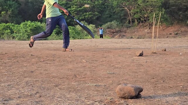 A batsman sprints in slow motion as a fast ball shatters branch-stick wickets in a rural field. This intense grassroots cricket match captures raw energy and high stakes, though lacks formal DRS tech.