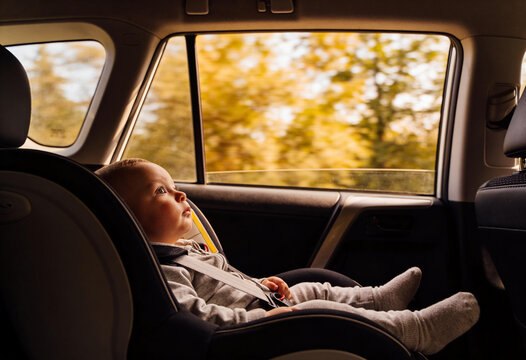 Baby boy sitting secured in a rear-facing car seat in the back seat during an autumn drive, child safety and family travel comfort