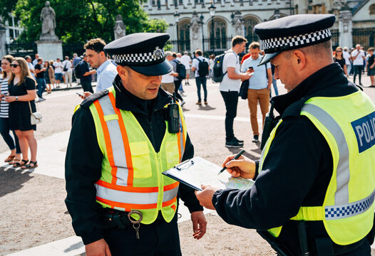Two British police officers reviewing a map on a clipboard at a busy outdoor public event in London, law enforcement coordination and crowd management on a sunny summer day