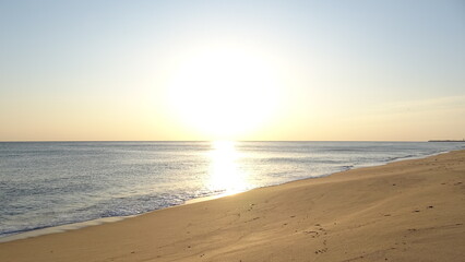 Obraz premium Bright Golden Morning Sun Over Empty Beach. A stunning, high-contrast shot of the bright morning sun reflecting on the wet sand and shoreline of a peaceful South Korean beach.