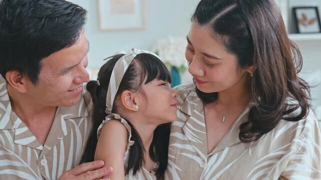 Slow motion Asian family slow motion mother kisses her daughter on the nose while the father smiles warmly, expressing love and bonding at home