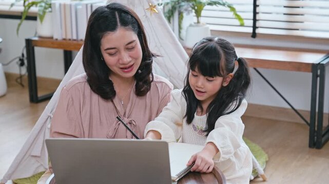 Asian family with mother teaching and helping her young daughter with writing and homework in a bright living room.