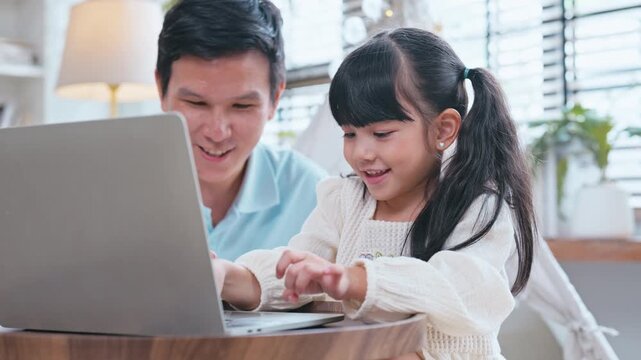 Asian family moment with father guiding his daughter through her school lessons and online learning on a laptop at home.