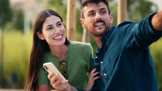 Video of lovely couple talking and laughing while looking together at smartphone in a park