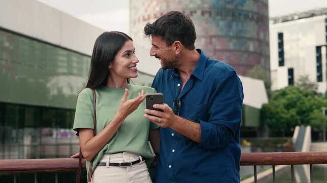 Video of lovely couple talking and laughing while looking together at smartphone in the city