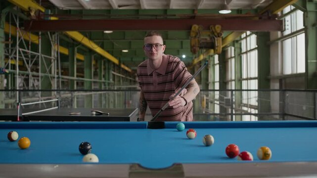 Front view eye level medium shot of young Caucasian man focusing and aiming cue ball while playing billiards in indoor setting