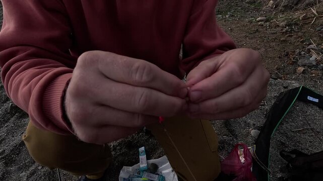 Fishing bait preparation, hands meticulously placing pink soft lure on a hook outdoors, hobby activity.