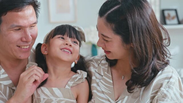 Cute Asian family portrait of father and mother expressing love by making a heart gesture on their daughter's smiling face.