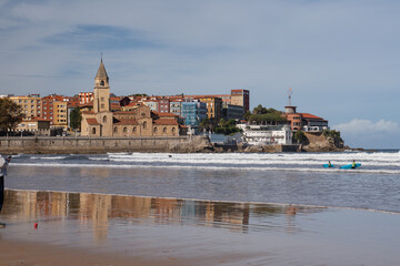 Obraz premium Panoramic view of San Lorenzo beach with San Pedro church reflection on wet sand. Gijon, Asturias, Northern Spain.