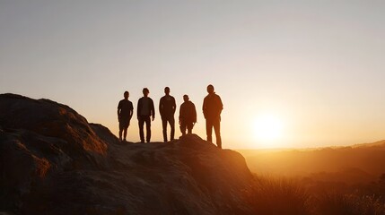 Fototapeta premium A small group of individuals stand silhouetted on a hilltop overlooking a vast warm illuminated landscape at sunset