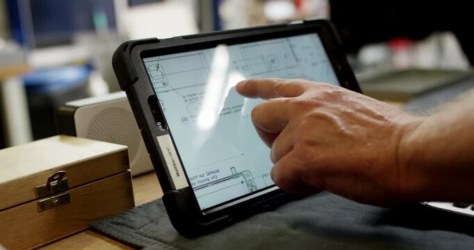 Close up of a technician hand interacting with a digital tablet displaying technical engineering plans