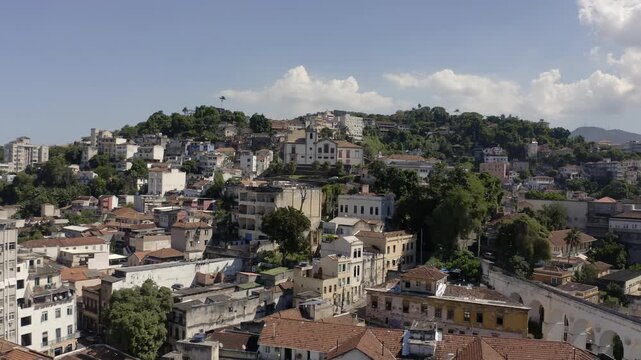 Drone Shot aerial view traveling in from Lapa neighborhood to historic region of Santa Teresa to church on top of the hill with houses  with mountains in background. City of Rio de Janeiro