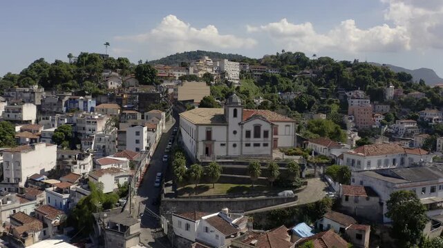 Drone Shot aerial view traveling out of church in top of the hill on historic region of Santa Teresa with houses and lapa with mountains in background. City of Rio de Janeiro