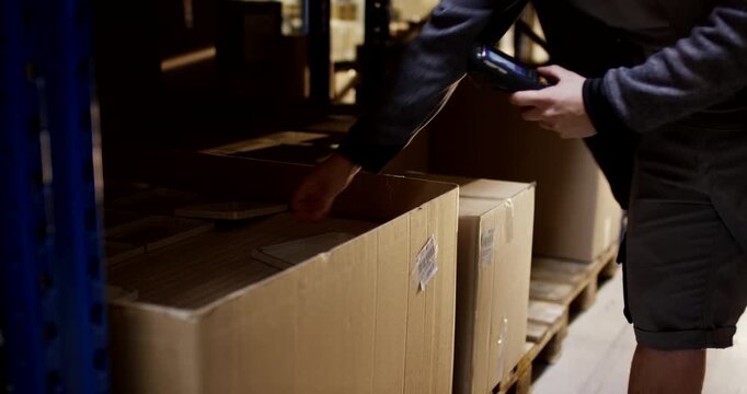 Warehouse worker using a handheld barcode scanner to check inventory in cardboard boxes on a pallet