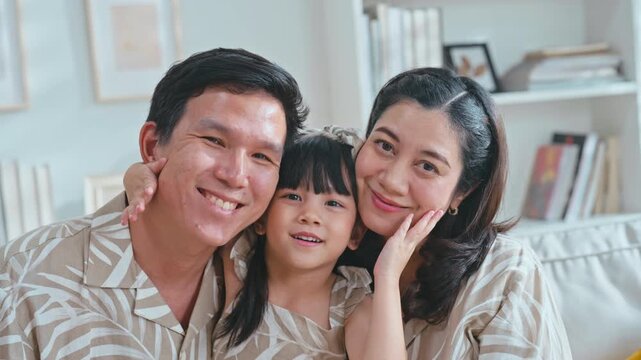 Slow motion Close-up portrait of happy Asian family father, mother, daughter smiling on living room sofa.