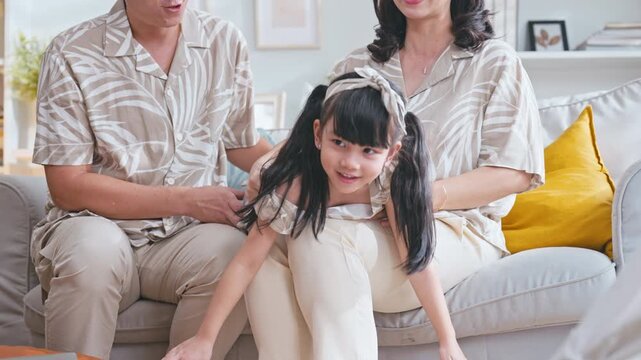 Asian family having fun as father and mother play with their daughter, pretending to fly an airplane on the couch and laughing.
