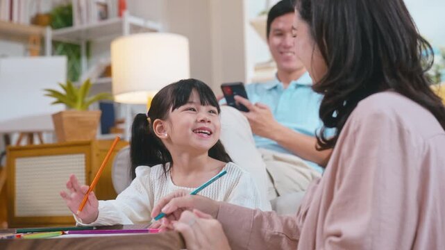 Asian family bonding as young daughter colors on paper with father and mother, encouraging creativity in their cozy living room.