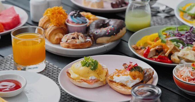 Assorted breakfast dishes including eggs benedict, pastries, and orange juice served on outdoor terrace, morning dining experience, hotel buffet catering background