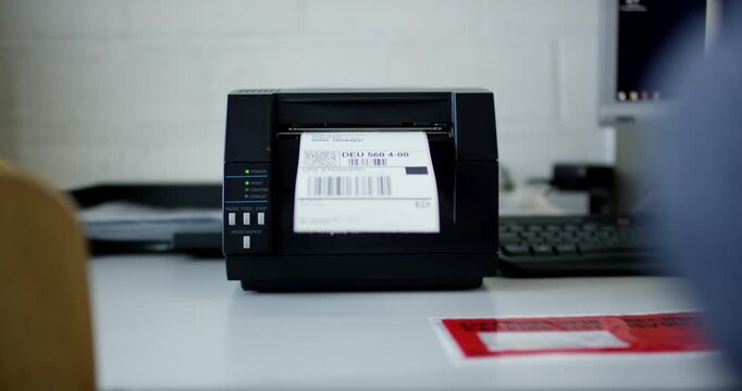 Industrial thermal label printer printing a shipping barcode label in a warehouse or office setting