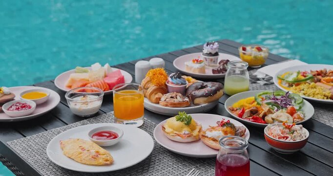 Breakfast dishes including omelet, eggs benedict, tropical fruit sitting on poolside table, turquoise swimming pool background, travel, luxury hospitality marketing