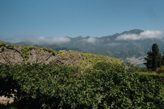 Panoramic mountain landscape of the Amalfi Coast with low clouds and lush greenery under a clear blue sky
