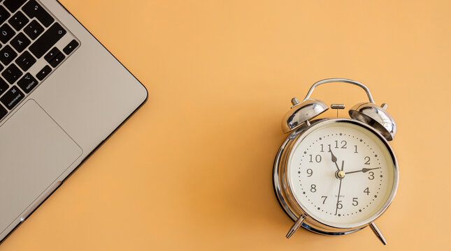Classic silver alarm clock and laptop on orange background for productivity and deadline concept.