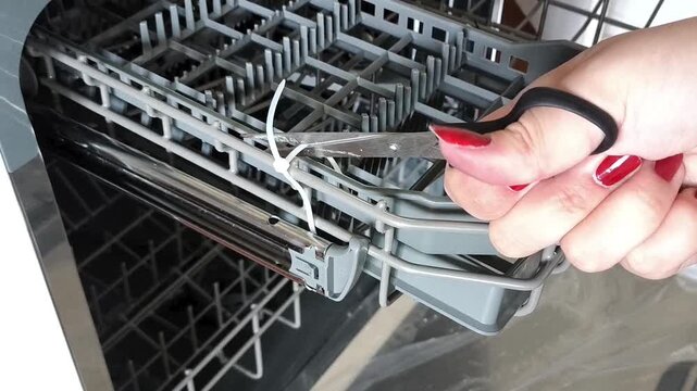 Cutting or removing packaging from dishwasher part. Preparing new kitchen appliance accessory for installation.