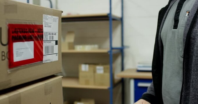 Warehouse worker hands attaching shipping label and packing list to cardboard box in distribution center