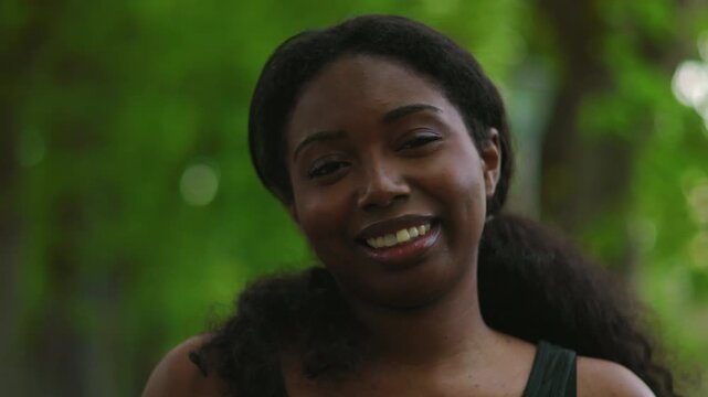 African American woman looking directly at camera with warm and natural smile creating friendly and engaging outdoor portrait moment in green environment