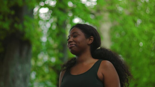 African American woman walking forward with confident and relaxed smile while camera tracks her movement creating dynamic and empowering outdoor lifestyle moment in green environment