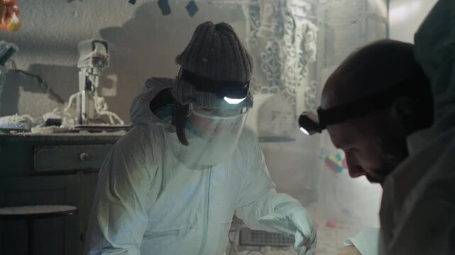 Caucasian technician and scientist in makeshift laboratory process contaminated sample under bright headlamp, careful pipette work, monitoring instruments on frostcoated bench, hushed collaborative