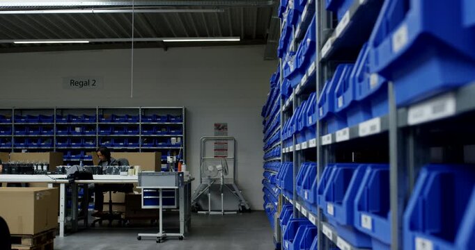 Warehouse worker at desk in storage facility with blue plastic bins on metal shelving units