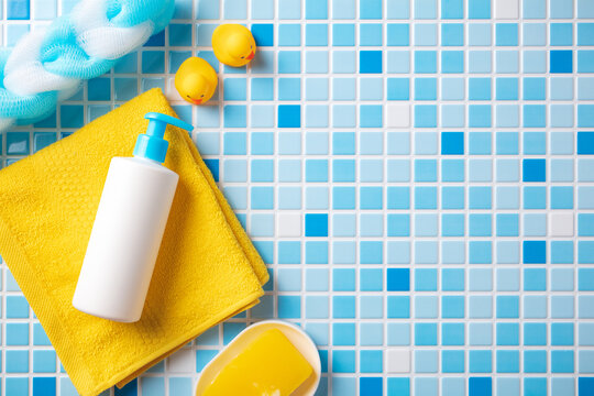 Baby shampoo bottle and yellow towel with rubber ducks on blue mosaic tiles background