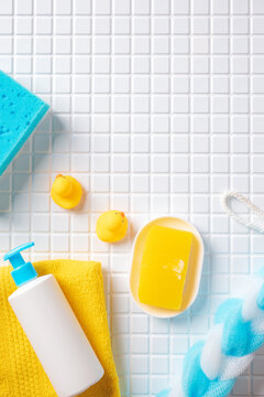 Top view of bathroom accessories with soap, pump bottle, and sponges on white tile background. Baby bath concept.