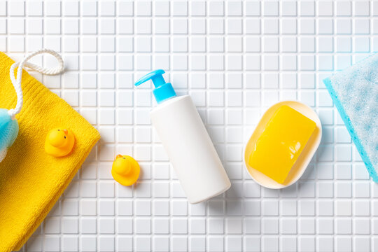 Baby bath products on white mosaic tiles table. Shampoo dispenser, soap, and yellow towel, washcloth and yellow rubber ducks