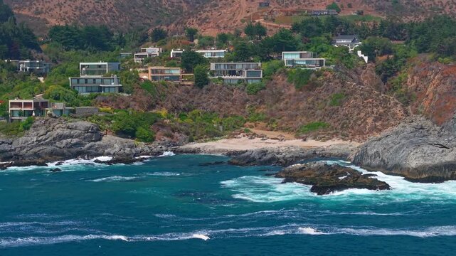 Aerial fly modern cliff side houses in Punta Pite beach Chile overlooking Pacific coastline with luxury coastal residences and rocky landscape