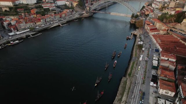 Douro River with Dom Luis I Bridge and rabelo boats in Porto municipality Porto district Norte region Portugal along Vila Nova de Gaia riverbank and urban waterfront, drone gliding forward