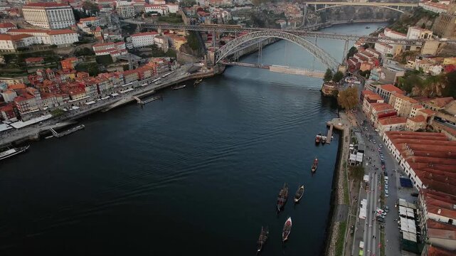 Douro River and Dom Luis I Bridge in Porto municipality Porto district Norte region Portugal with rabelo boats along Vila Nova de Gaia riverbank and waterfront road, drone gliding forward