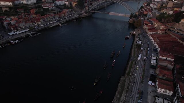 Douro River and Dom Luis I Bridge in Porto municipality Porto district Norte region Portugal with rabelo boats along Vila Nova de Gaia riverbank, drone gliding forward and tilting camera up