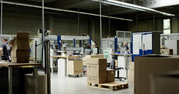 Industrial workers operating machinery and packing cardboard boxes in a large manufacturing facility